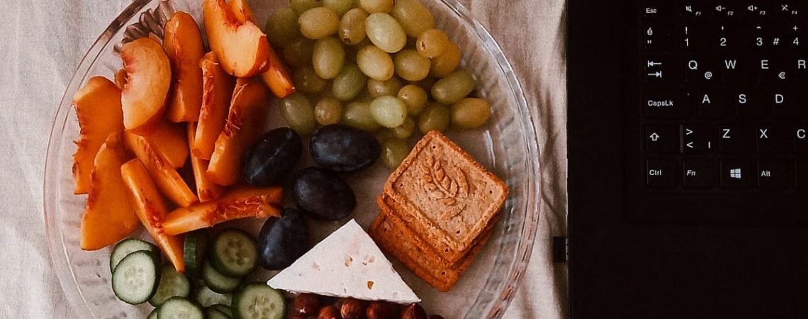 A delightful snack plate with fruits, cheese, and a laptop for a healthy lifestyle.